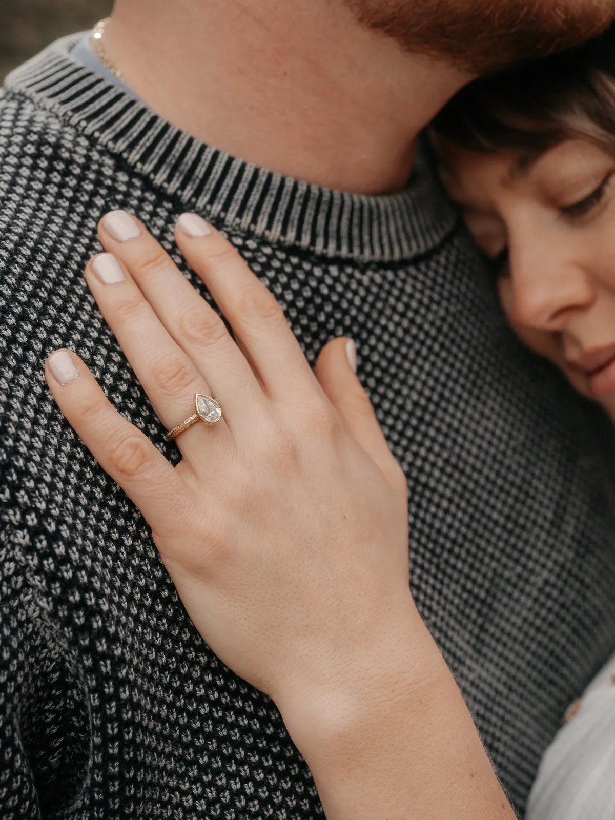 A woman wearing a pear-shaped diamond engagement ring embraces her partner