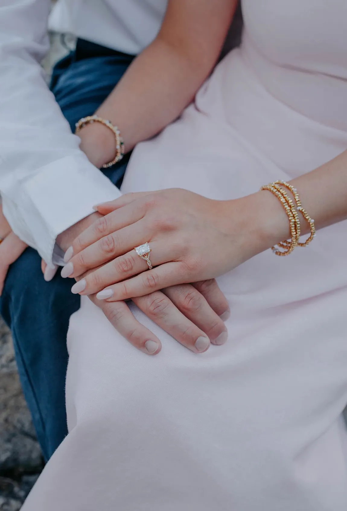 Couple's hands with engagement ring and bracelets on a pink dress.
