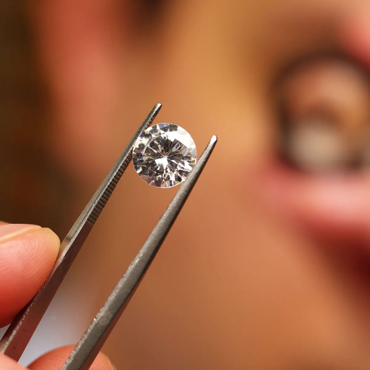 A diamond held by tweezers, with a blurred background.