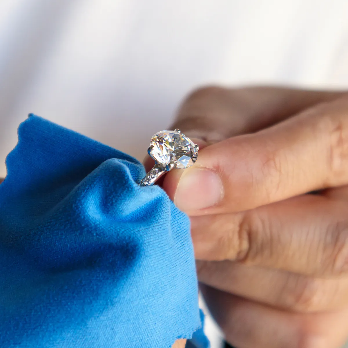 A hand cleaning a diamond ring with a blue cloth.