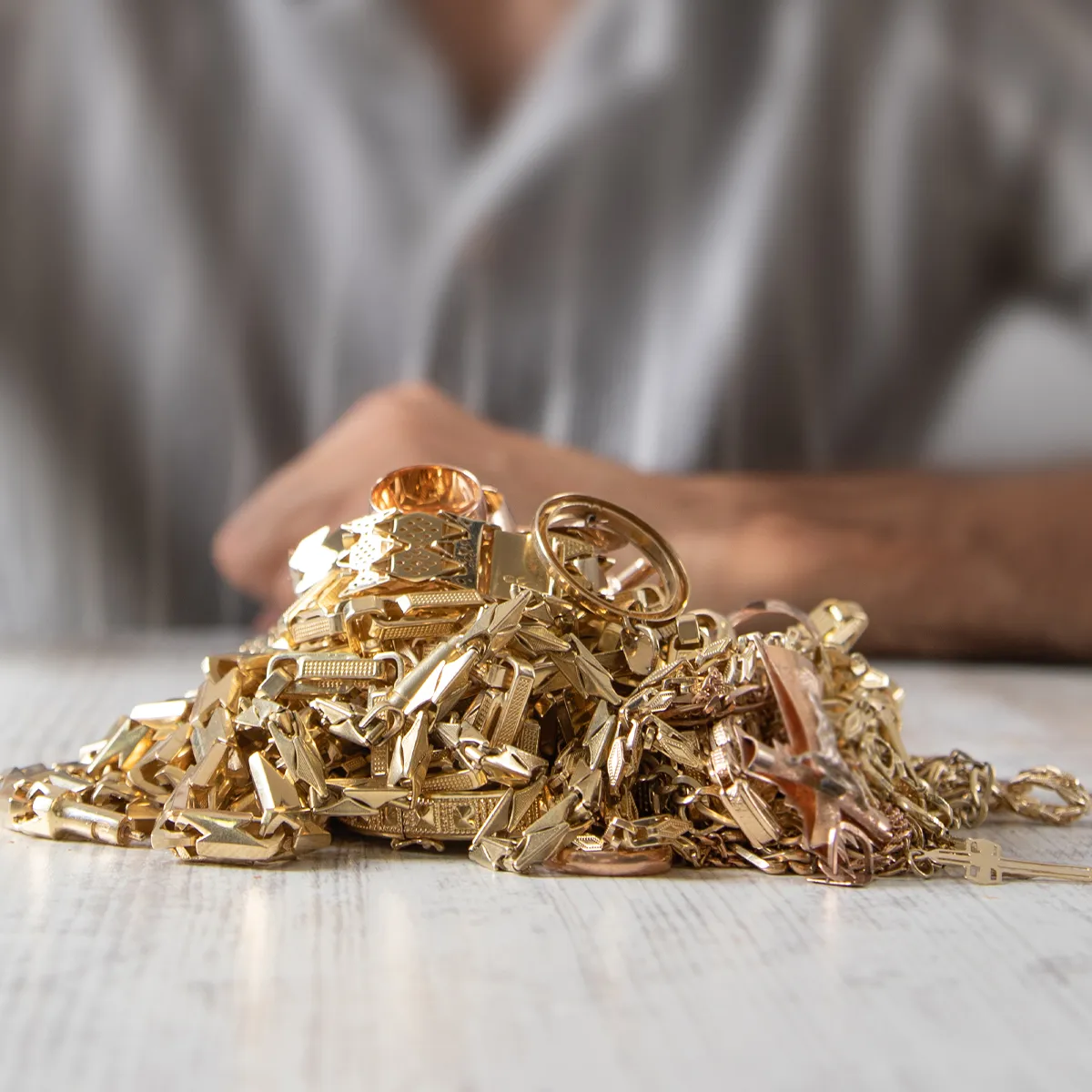 A pile of gold jewelry, including chains and rings, on a table with a blurred person in the background.