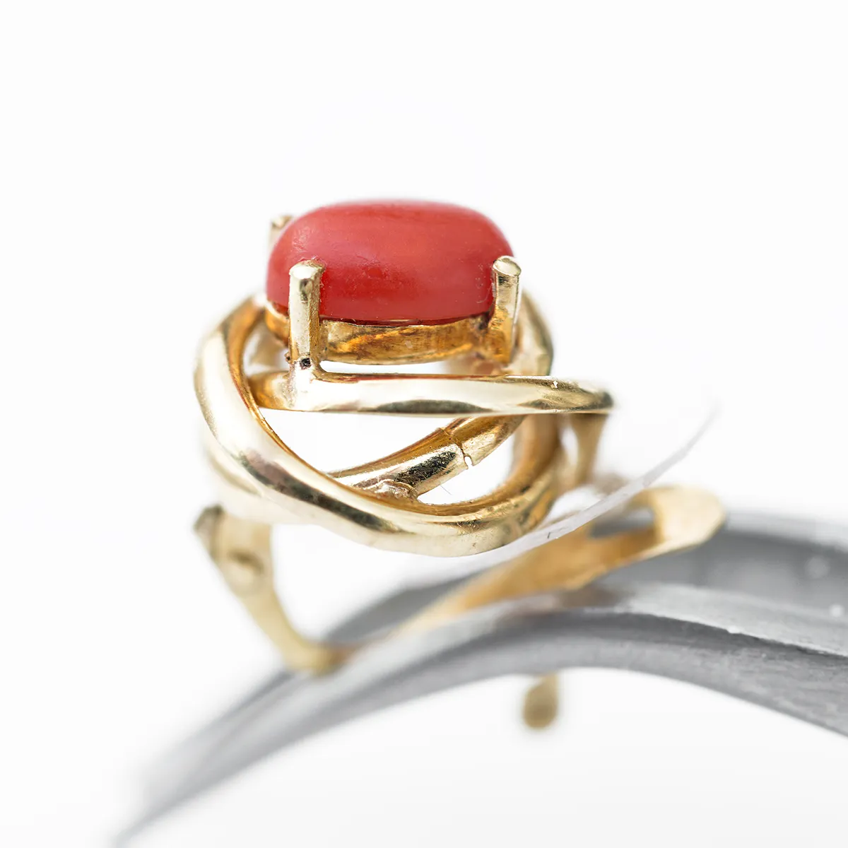 A gold ring with a red gemstone in a unique, intertwined design.