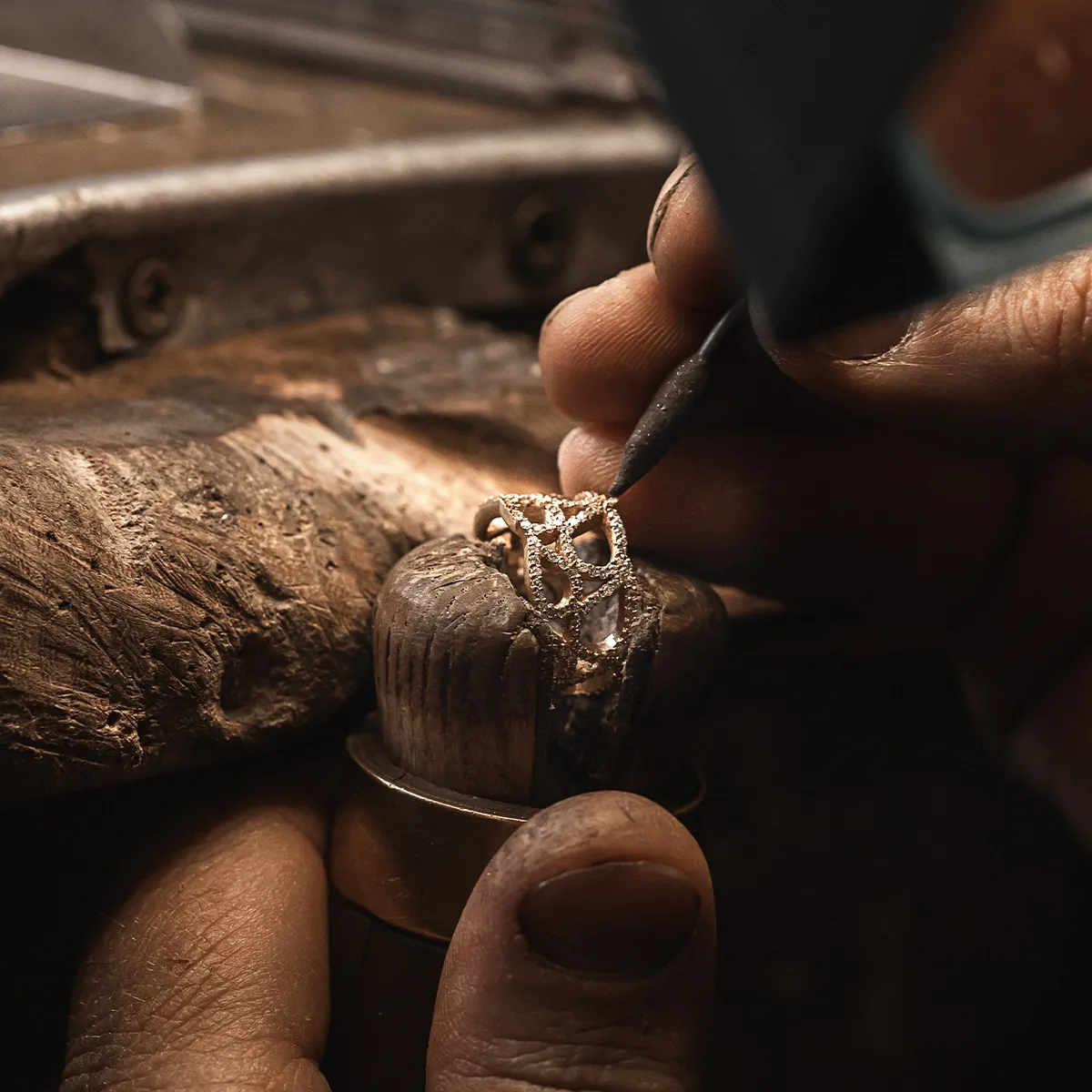 A jeweler's hands working on a ring with a tool on a wooden workbench.
