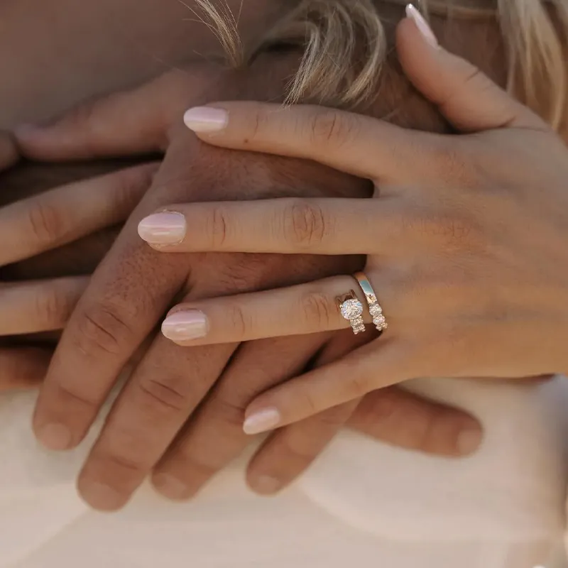 Two hands with rings, one with a diamond engagement ring, resting on another person's hand.