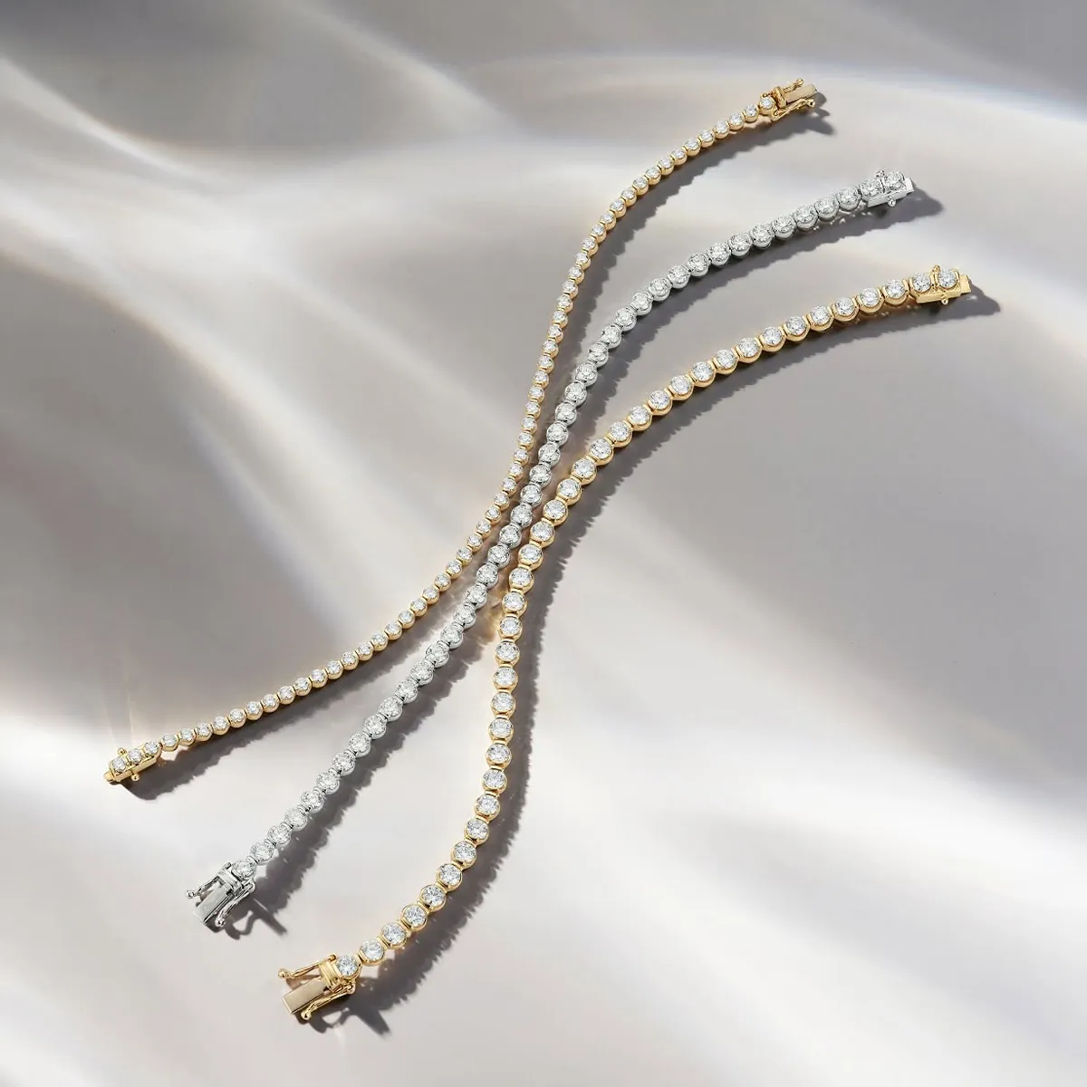 Elegant gold and silver tennis bracelets with diamonds on a soft, wavy background. Explore more at Midtown Jewelers.