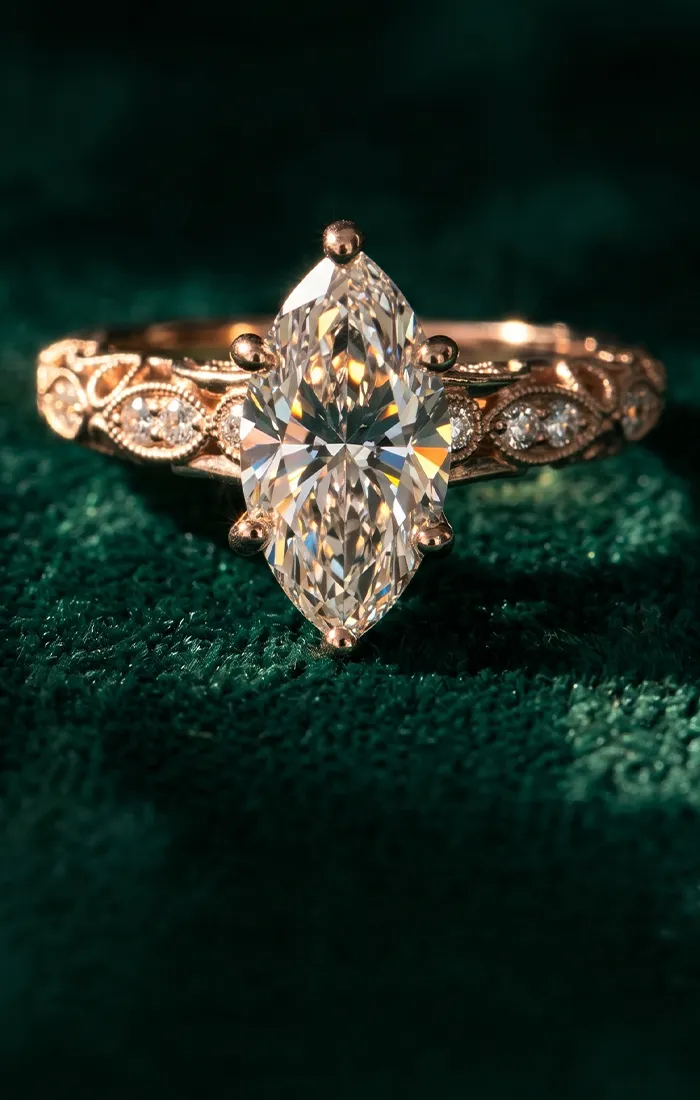 Elegant marquise diamond ring with intricate gold band on green velvet background.