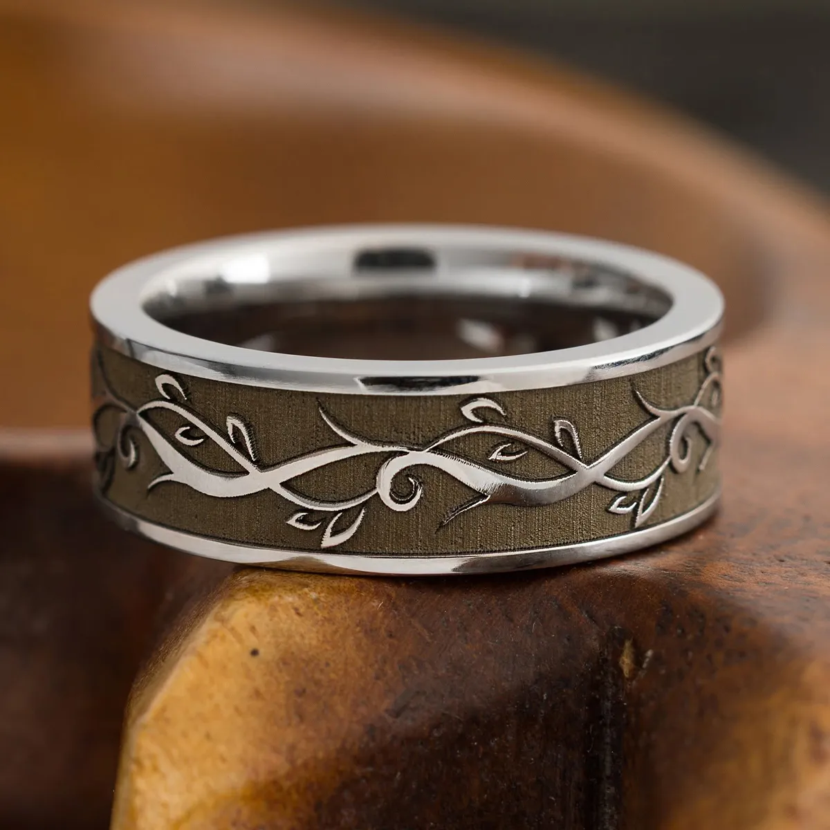 Silver ring with vine design on wooden surface. Explore wedding rings at Midtown Jewelers.