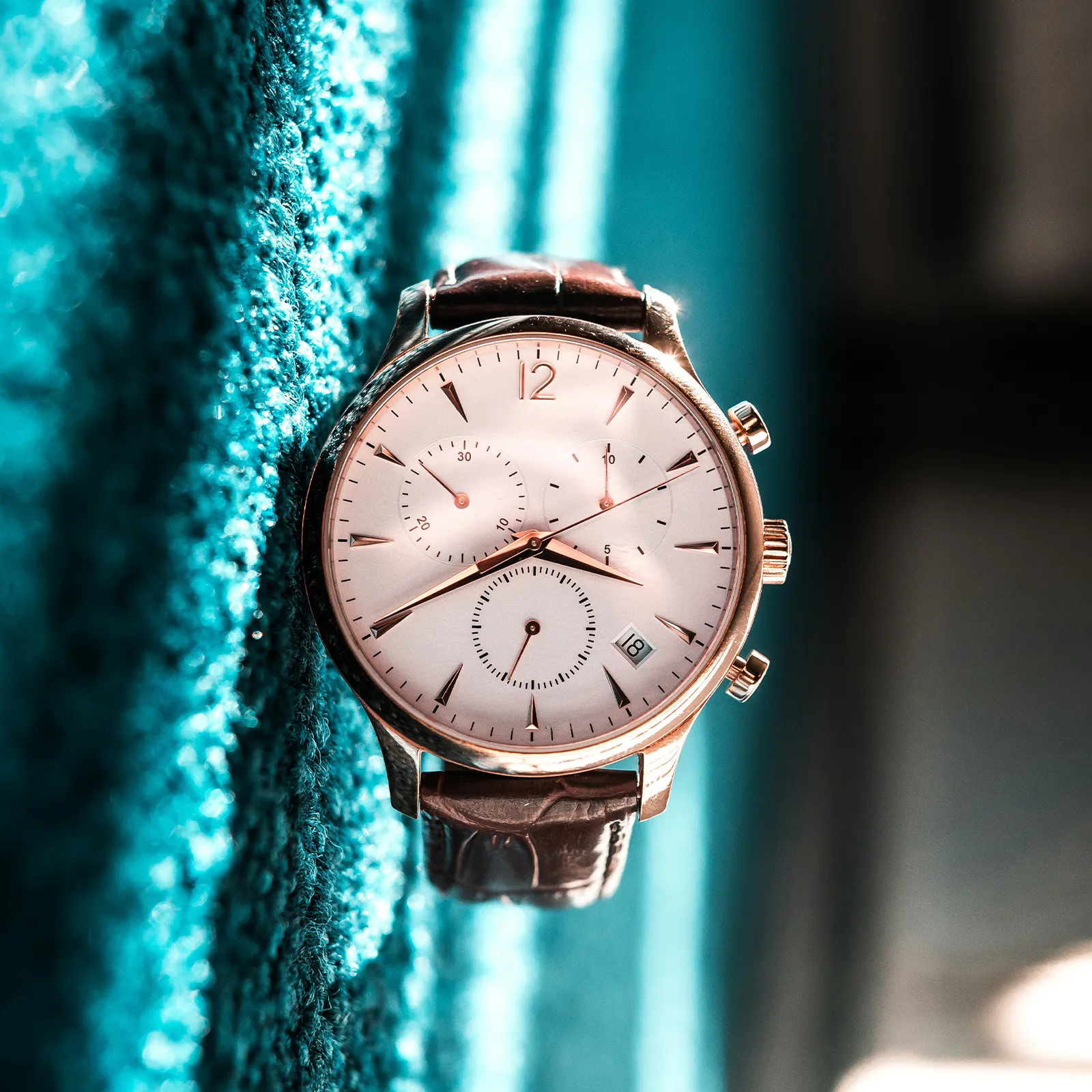 Luxury watch with leather strap on textured teal background. Click to browse Capitol Time.