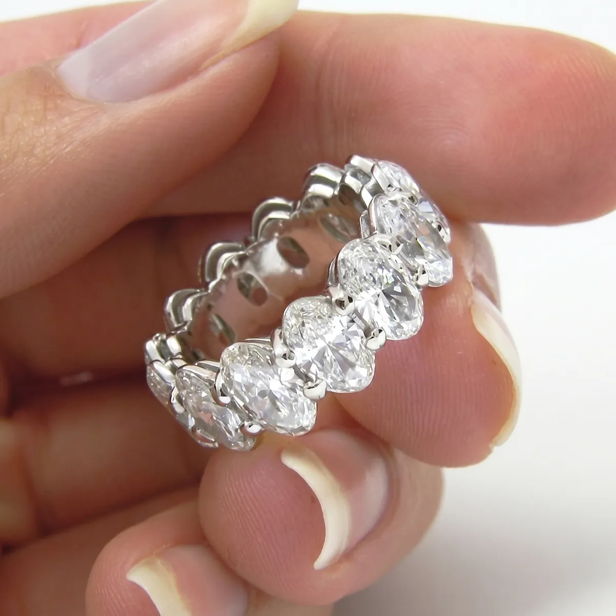 A hand holding a silver ring with large, oval-cut diamonds encircling it.
