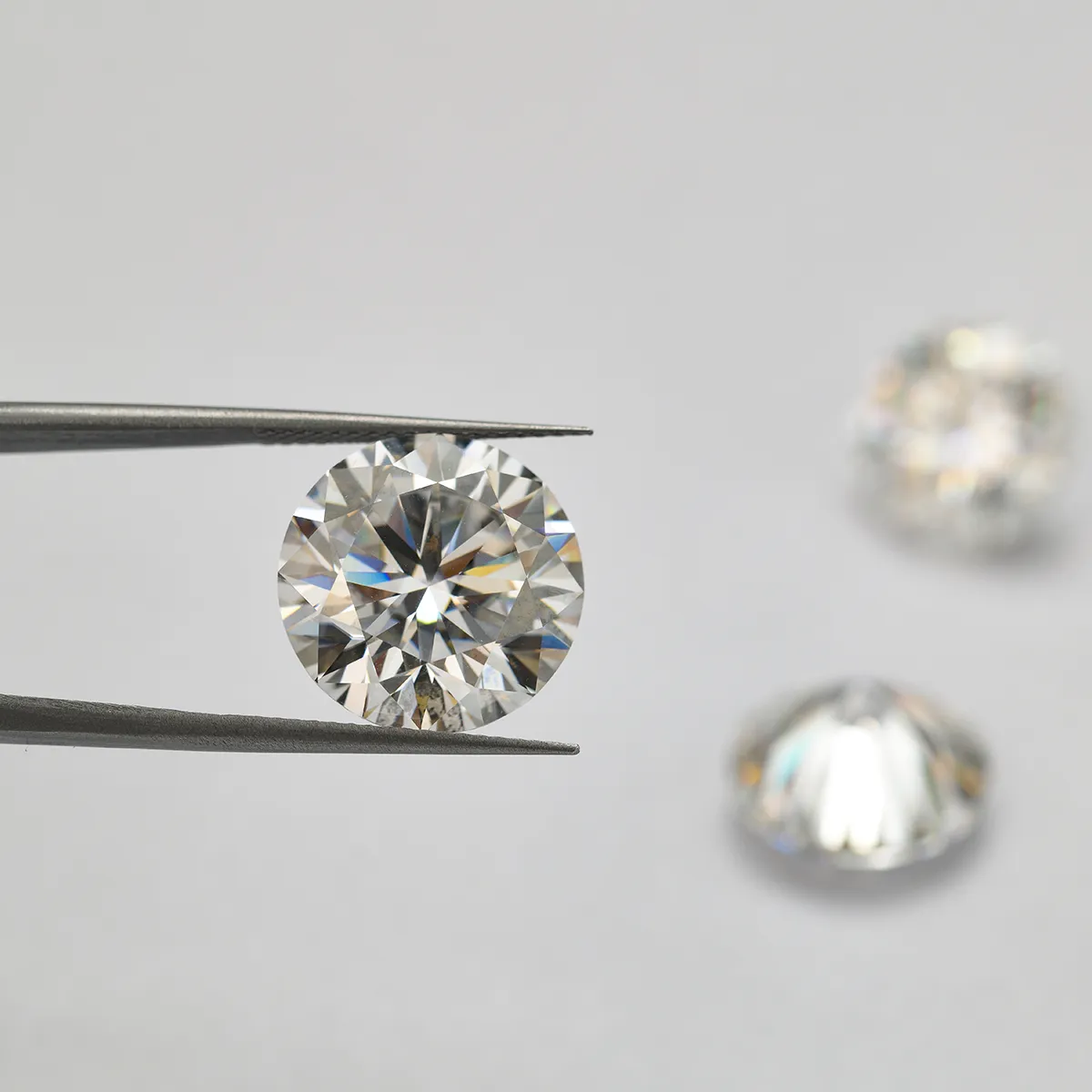 Diamond held by tweezers with two more in the background. Shop loose diamonds at Midtown Jewelers in Herndon, VA.