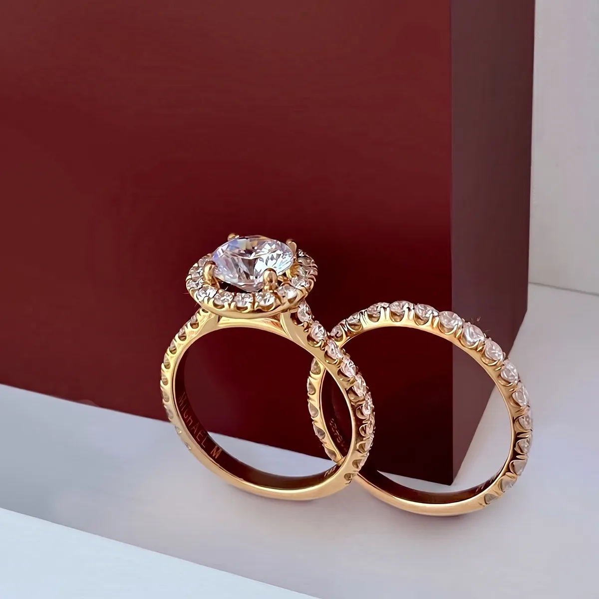 Gold engagement ring set with diamonds against a red background.