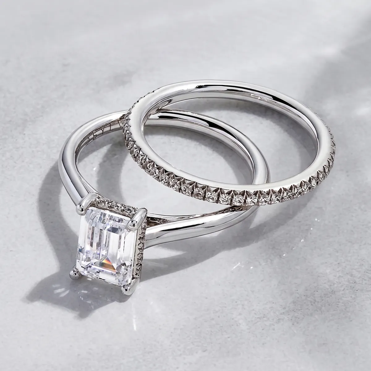 Two silver rings, one with an emerald-cut diamond, the other with small diamonds, on a light surface.