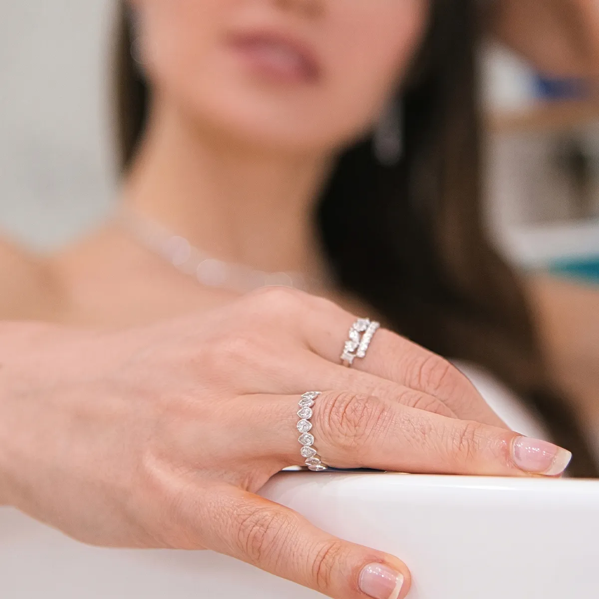 Close-up of a woman's hand wearing two diamond rings, with a blurred background.