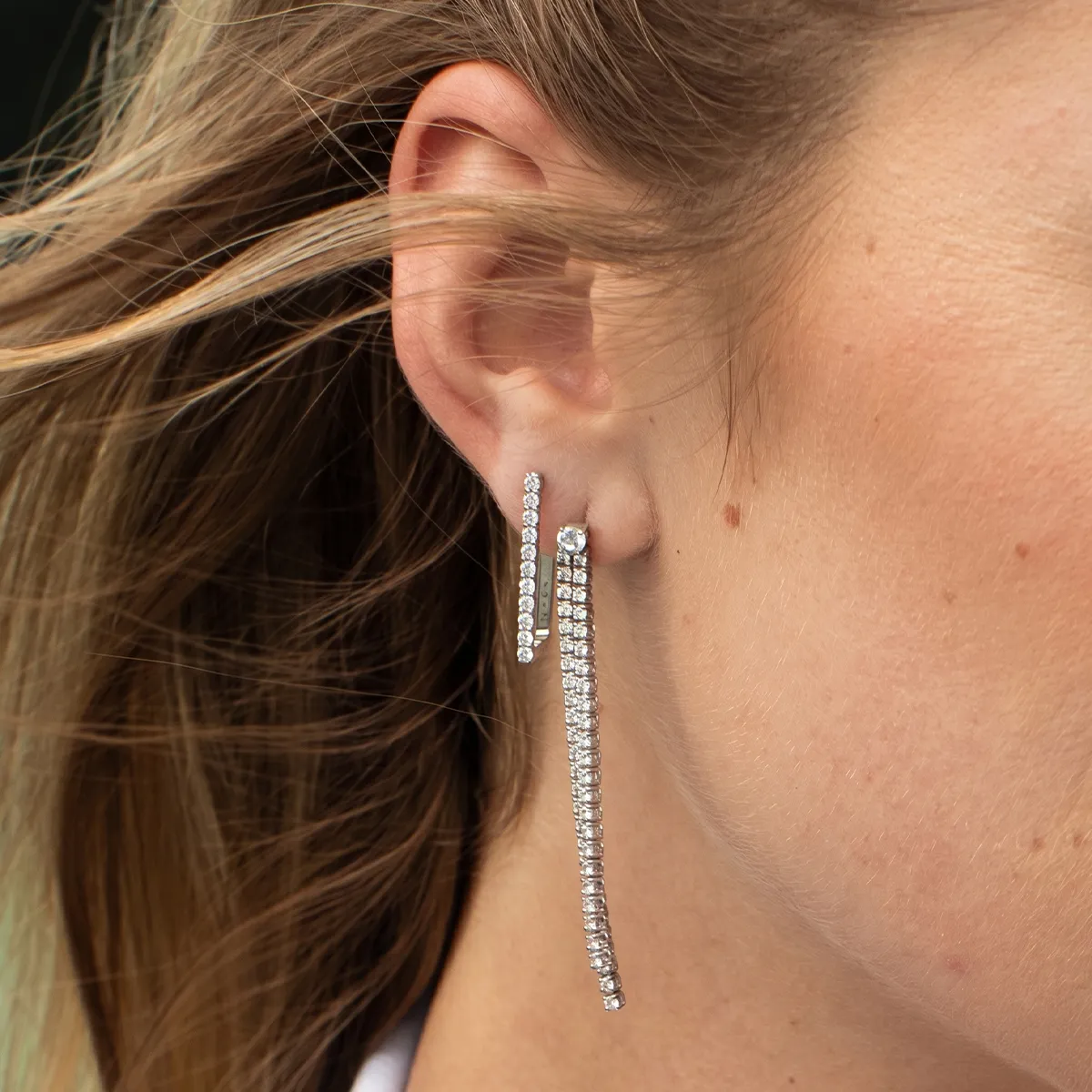 Close-up of a woman's ear wearing elegant, long, sparkling earrings.