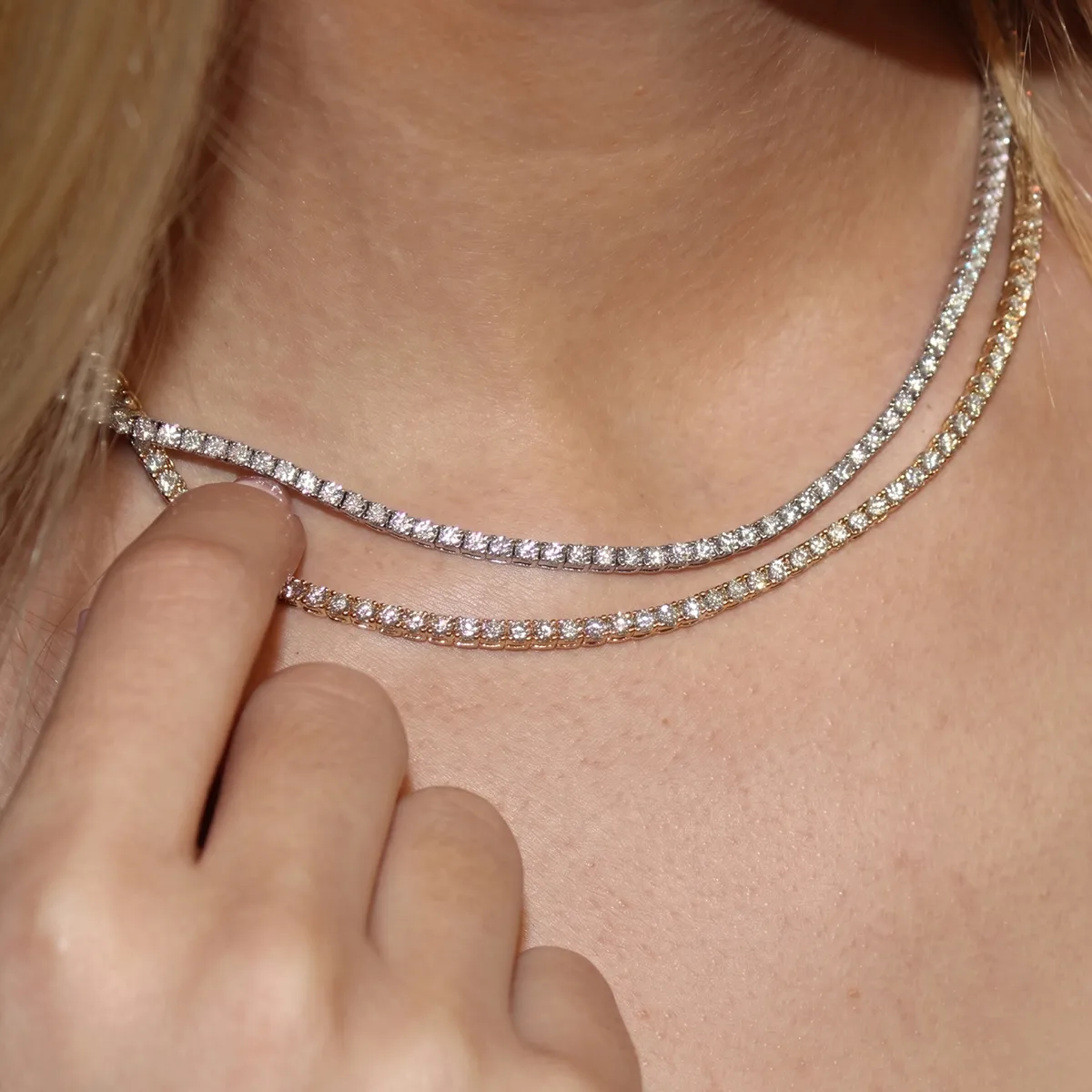A person wearing two sparkling diamond necklaces, one gold and one silver, with a hand touching them.