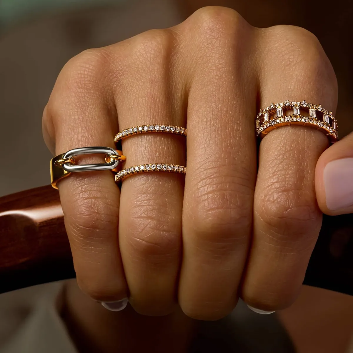 Hand with four gold and diamond rings, showcasing elegant jewelry designs.