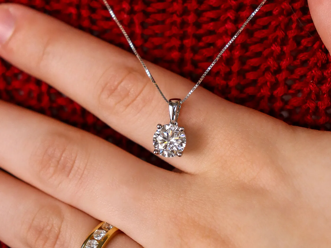Close-up of a hand wearing a diamond pendant necklace and a gold ring. Click to shop necklaces at Miner's Den Jewelers.