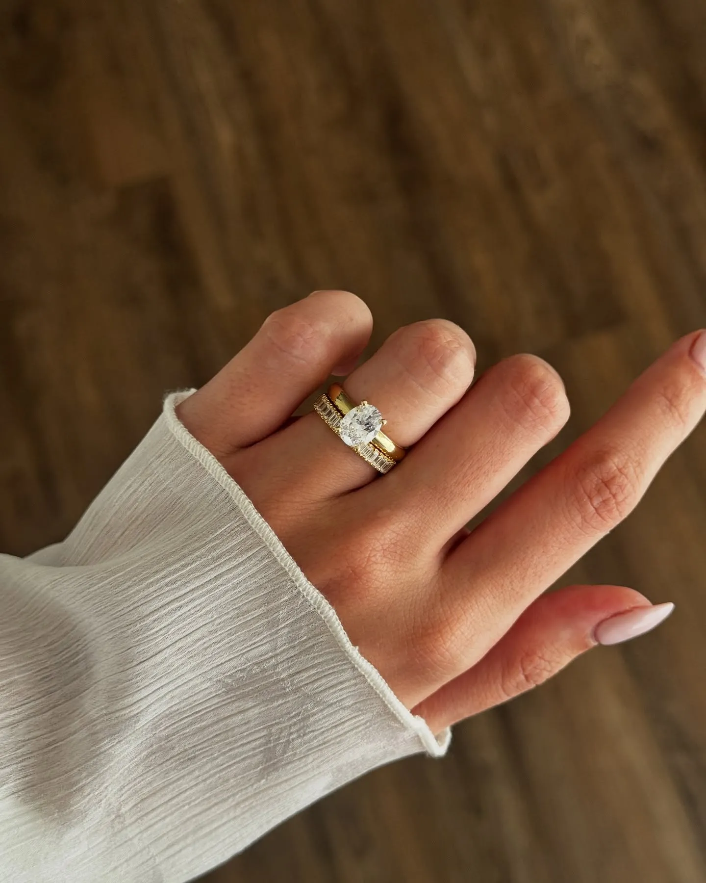 Hand with pink nails wearing a diamond cross ring on a floral dress background.
