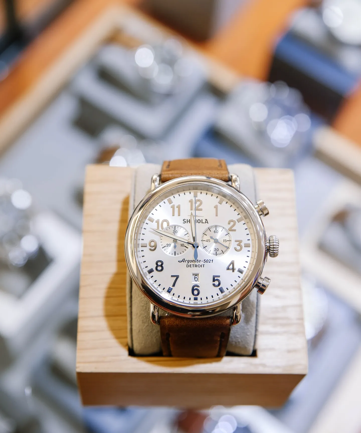 Silver watch with brown leather strap displayed on a wooden stand.