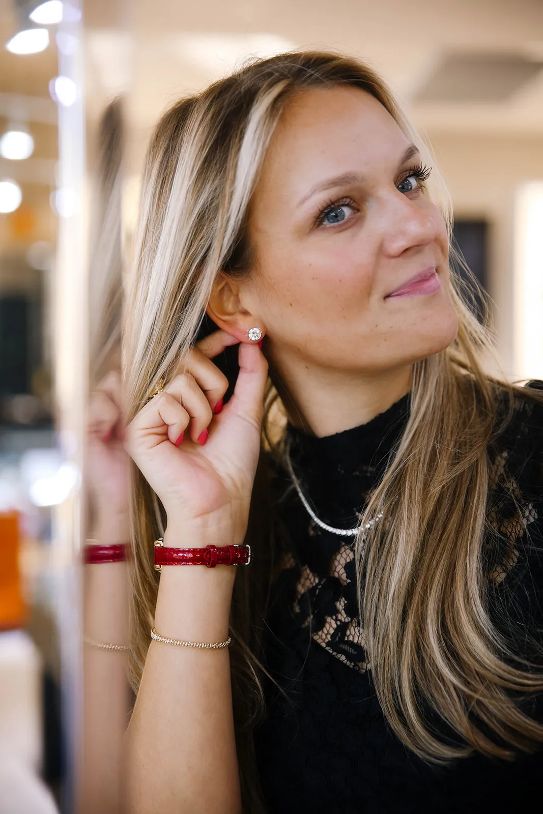 Woman trying on a diamond earring, wearing a red watch and black lace top.