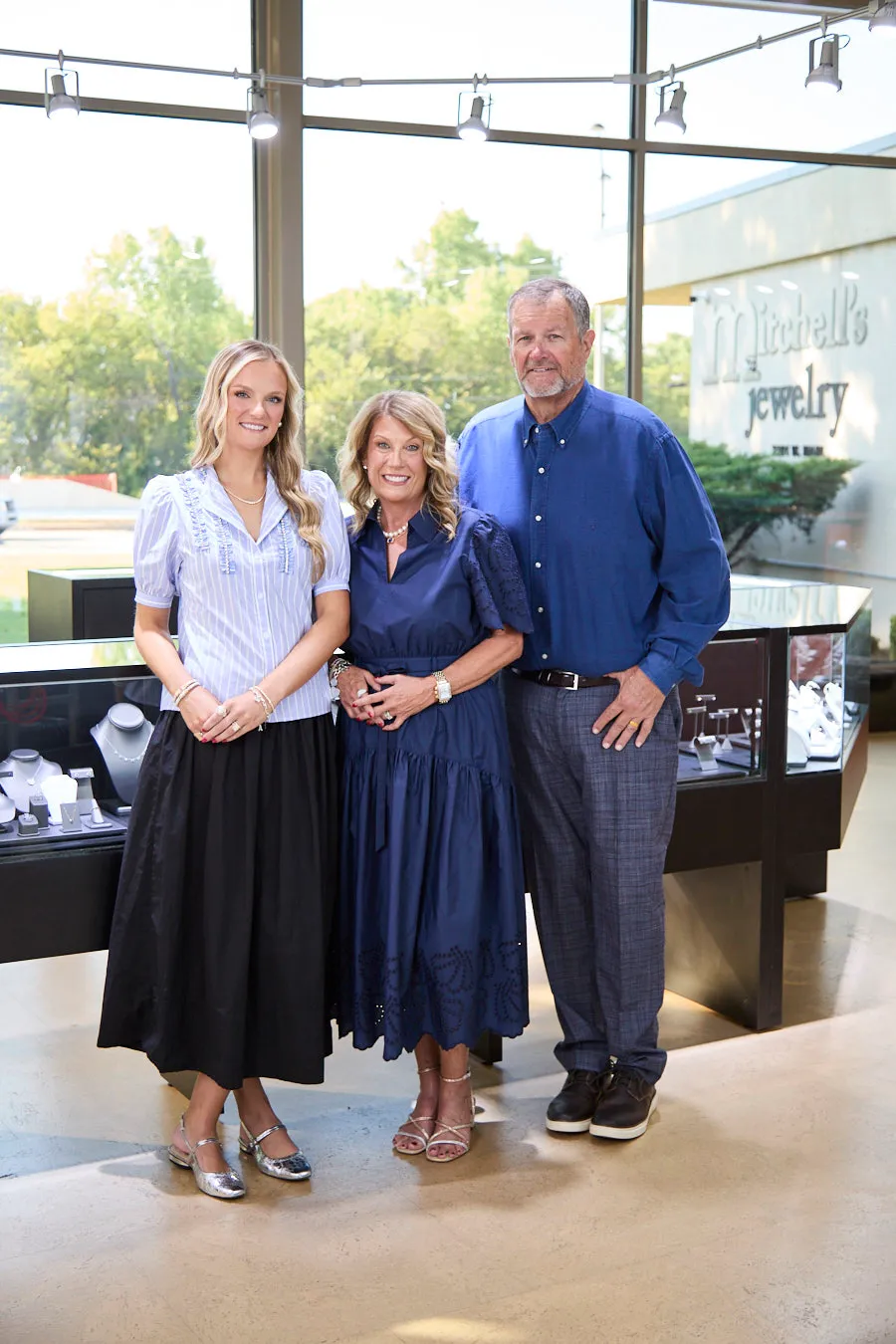 Three people smiling inside Mitchell's Jewelry store, standing near display cases.