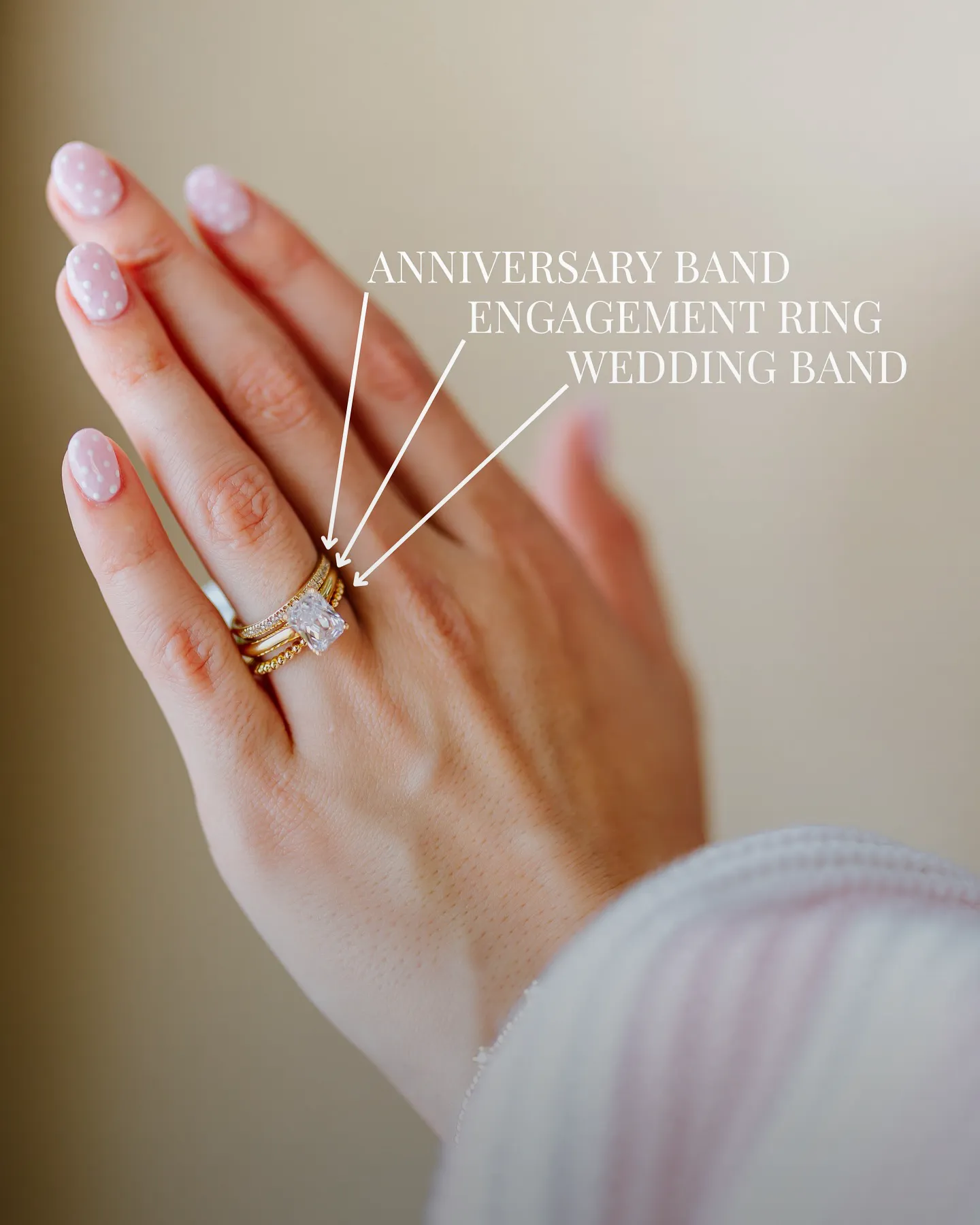 A hand with pink polka dot nails wearing an anniversary band, engagement ring, and wedding band.
