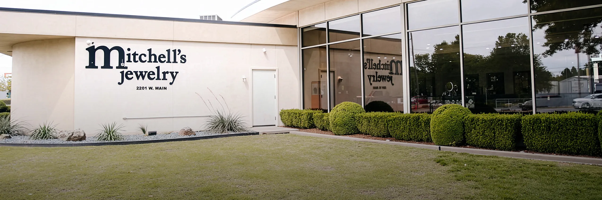 Modern jewelry store exterior with large windows and manicured shrubs. View store information.