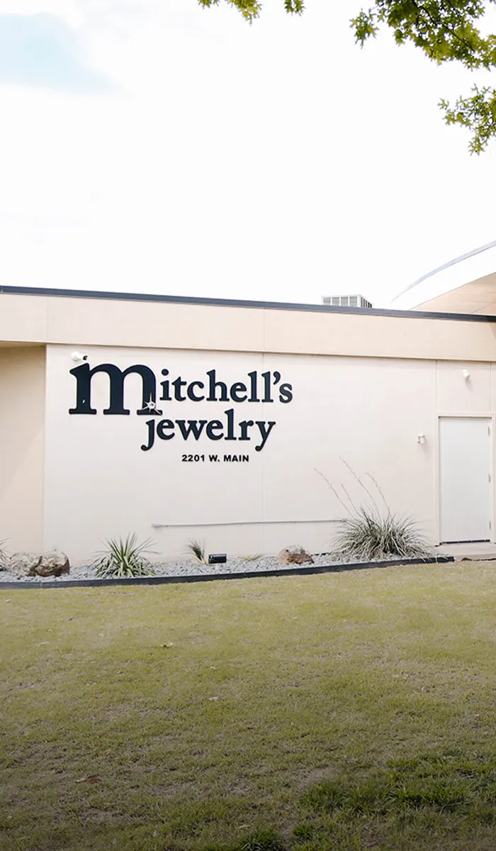 Modern jewelry store exterior with large windows and manicured shrubs. View store information.