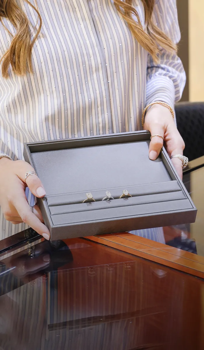 Person holding a tray with rings at a jewelry store. Book a Consultation.