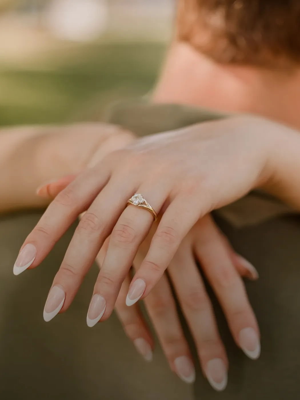 Close-up of hands with a diamond ring on finger, resting on someone's shoulder.