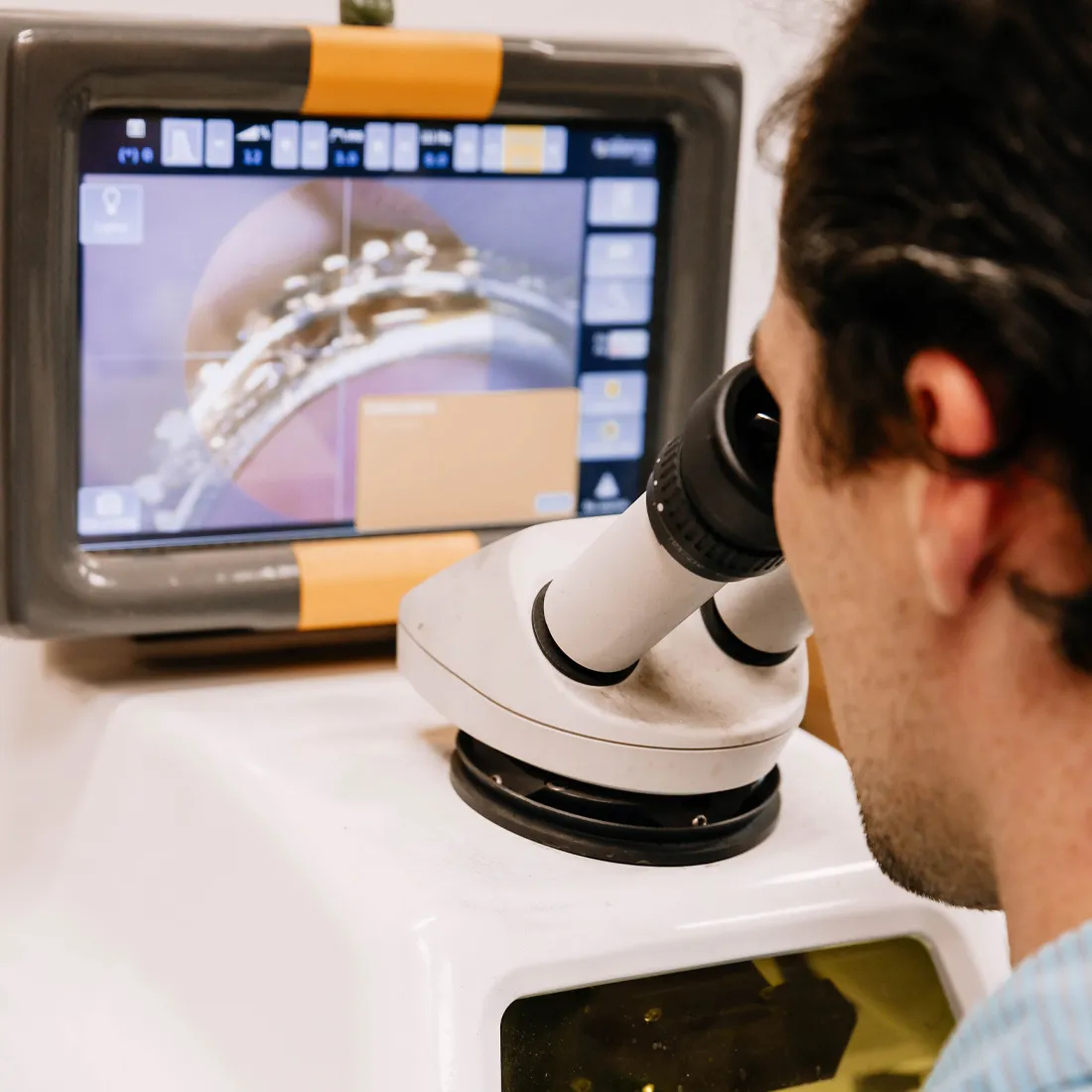 Person using a microscope with a digital display showing a magnified image.