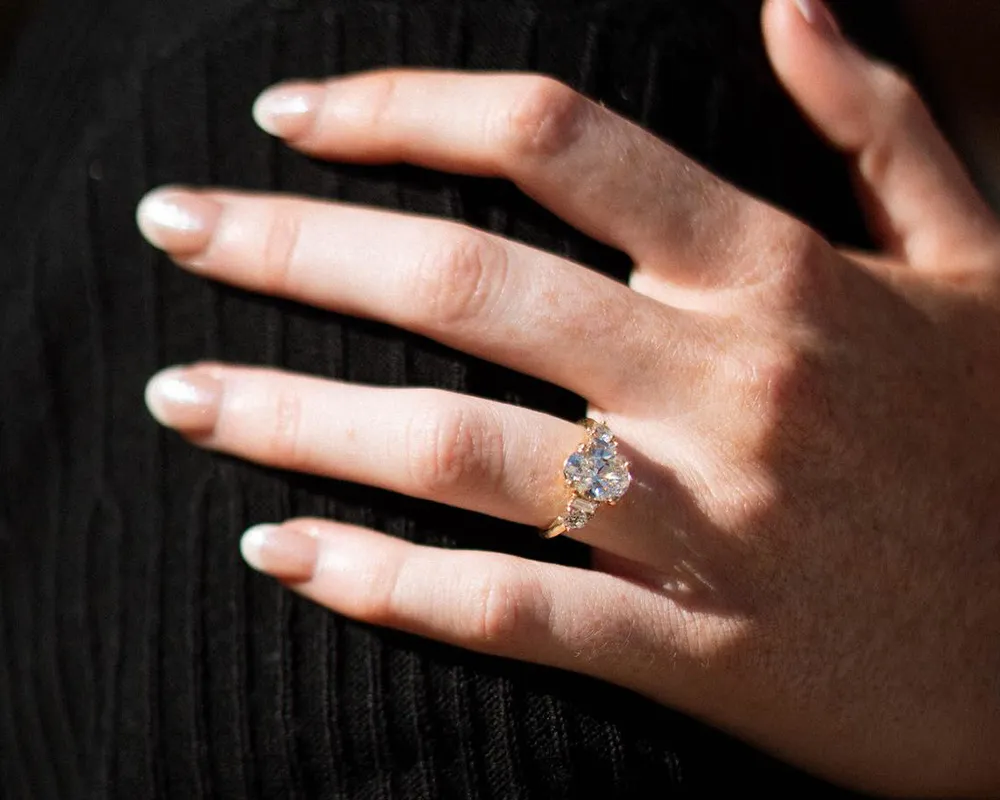 A hand with a large diamond ring on a black background.