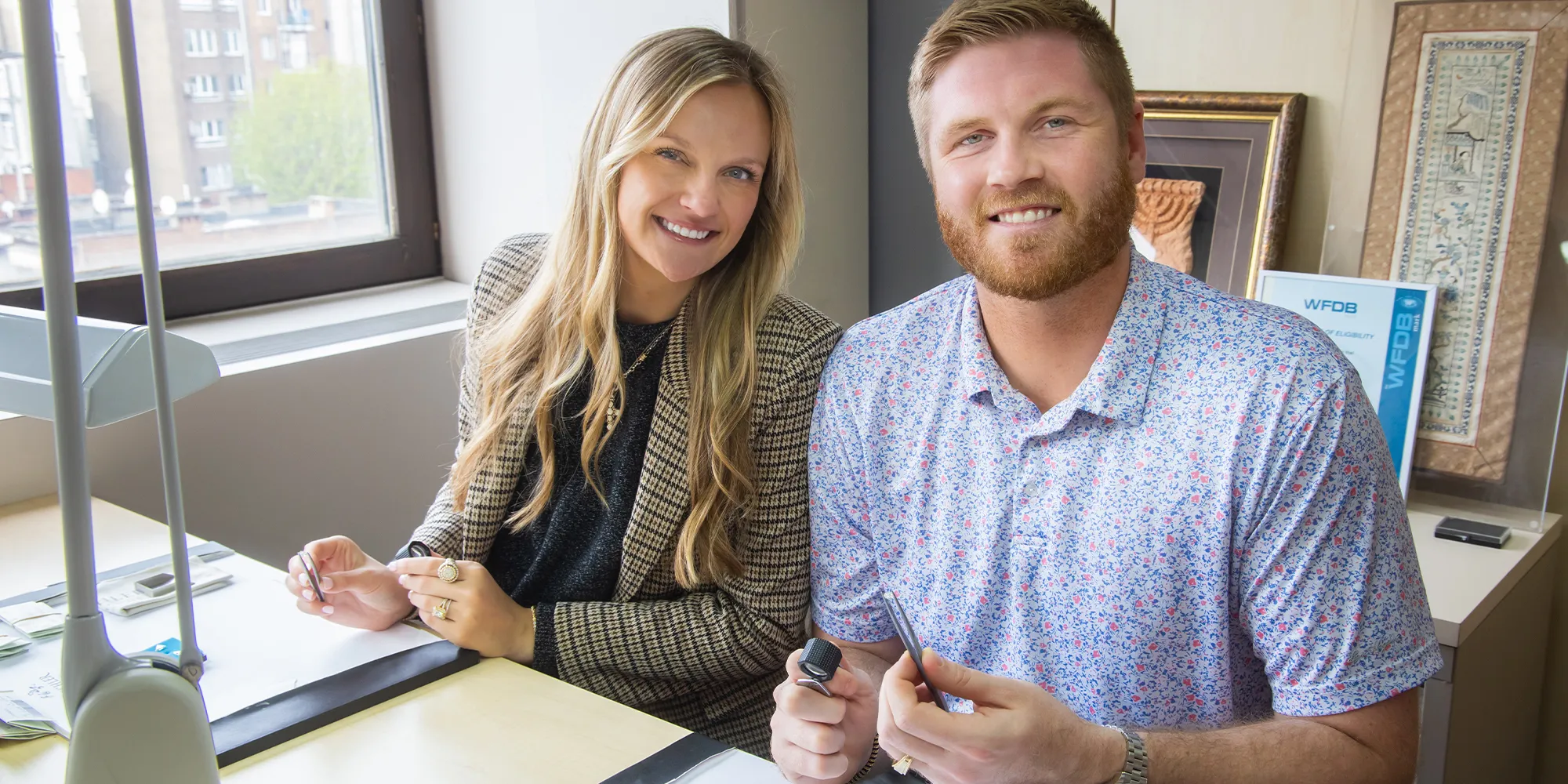 A man and woman smiling, holding jewelry tools, in a bright room.