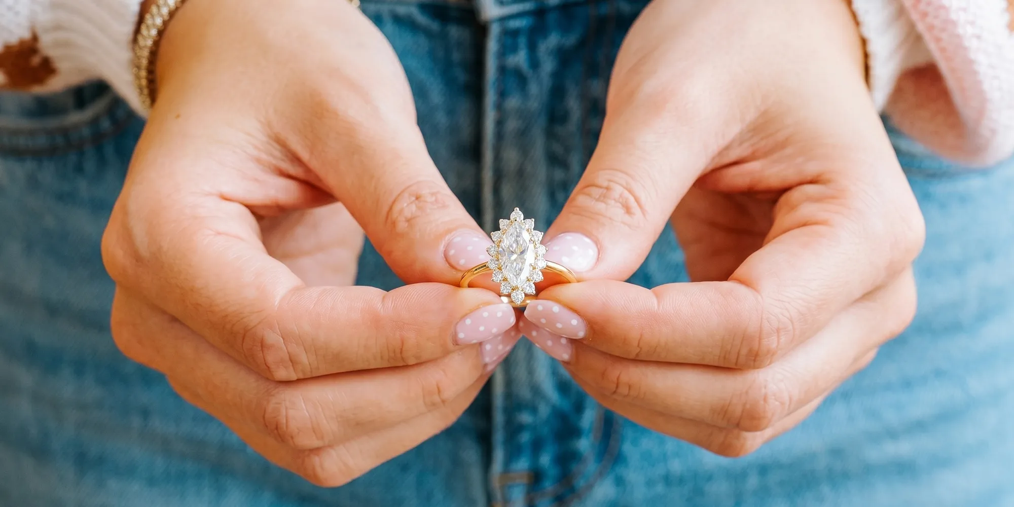 Hands holding a gold ring with a large marquise diamond and halo setting.