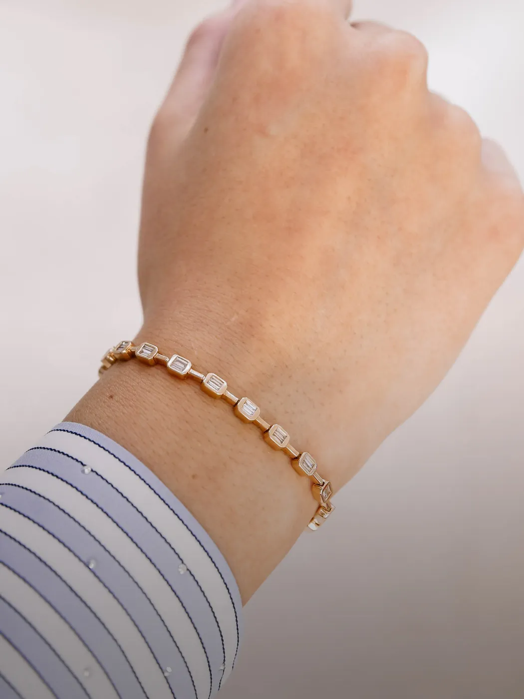 A hand wearing a gold bracelet with rectangular links, against a light background.