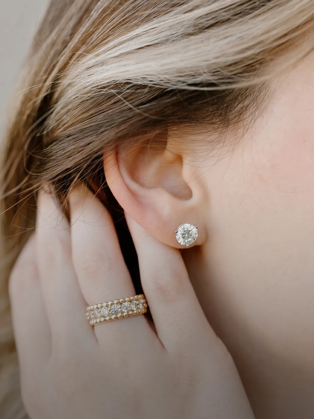 Close-up of a person wearing a diamond stud earring and a gold ring with diamonds.