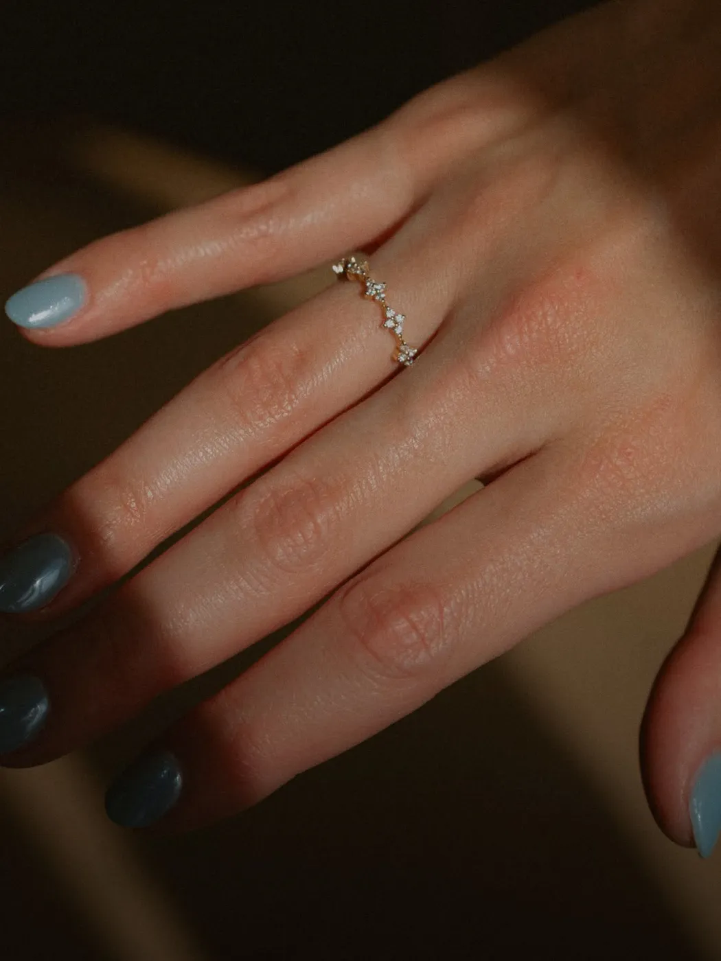 Hand with blue nails wearing a delicate gold ring with small diamonds.
