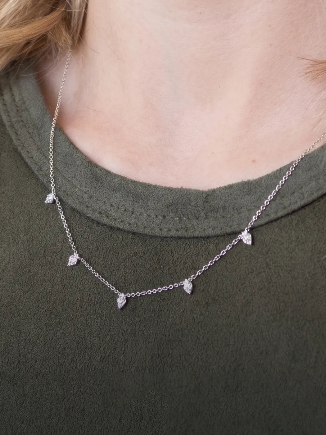 Silver necklace with small diamond-shaped pendants on a person wearing a green top.