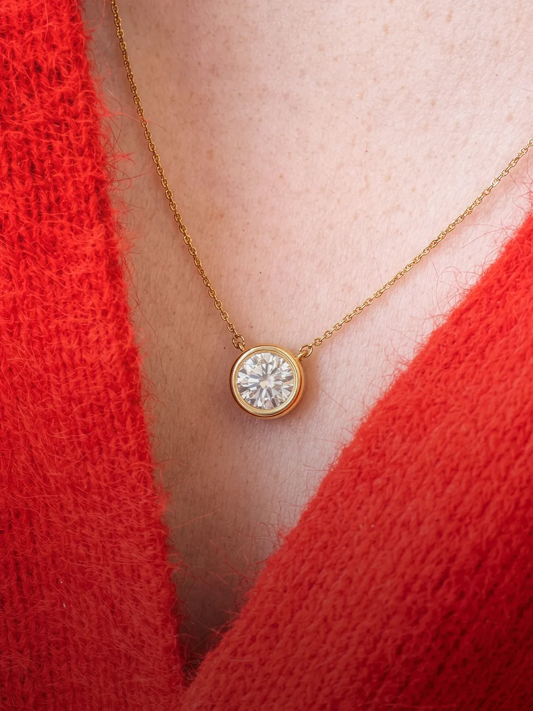 Gold chain necklace with a round diamond pendant against a red sweater.