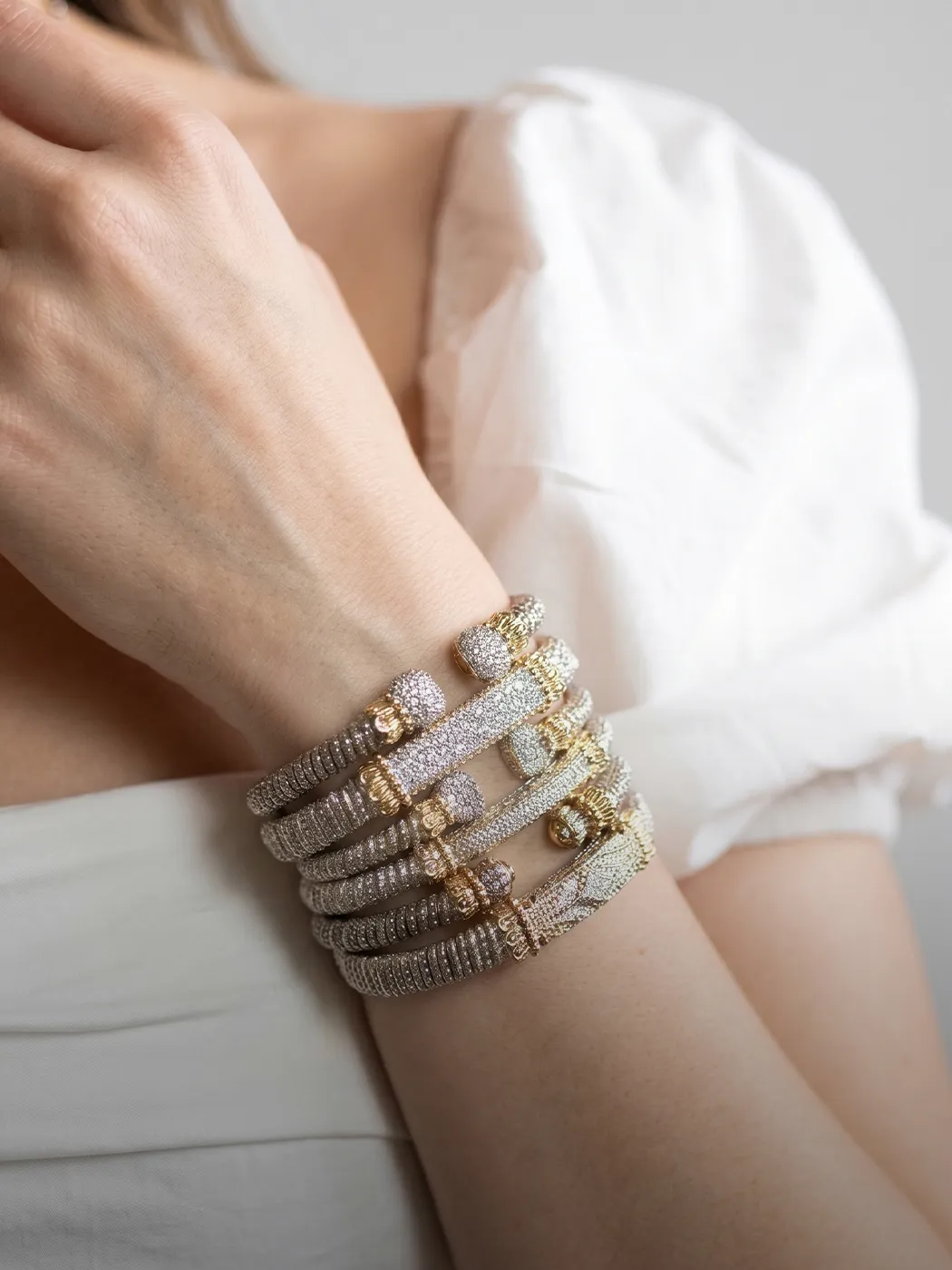 A person wearing multiple diamond and gold bracelets on their wrist.