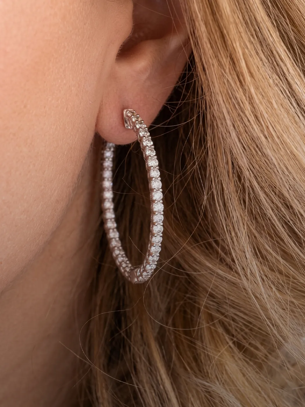 Diamond hoop earring worn on ear with blonde hair.