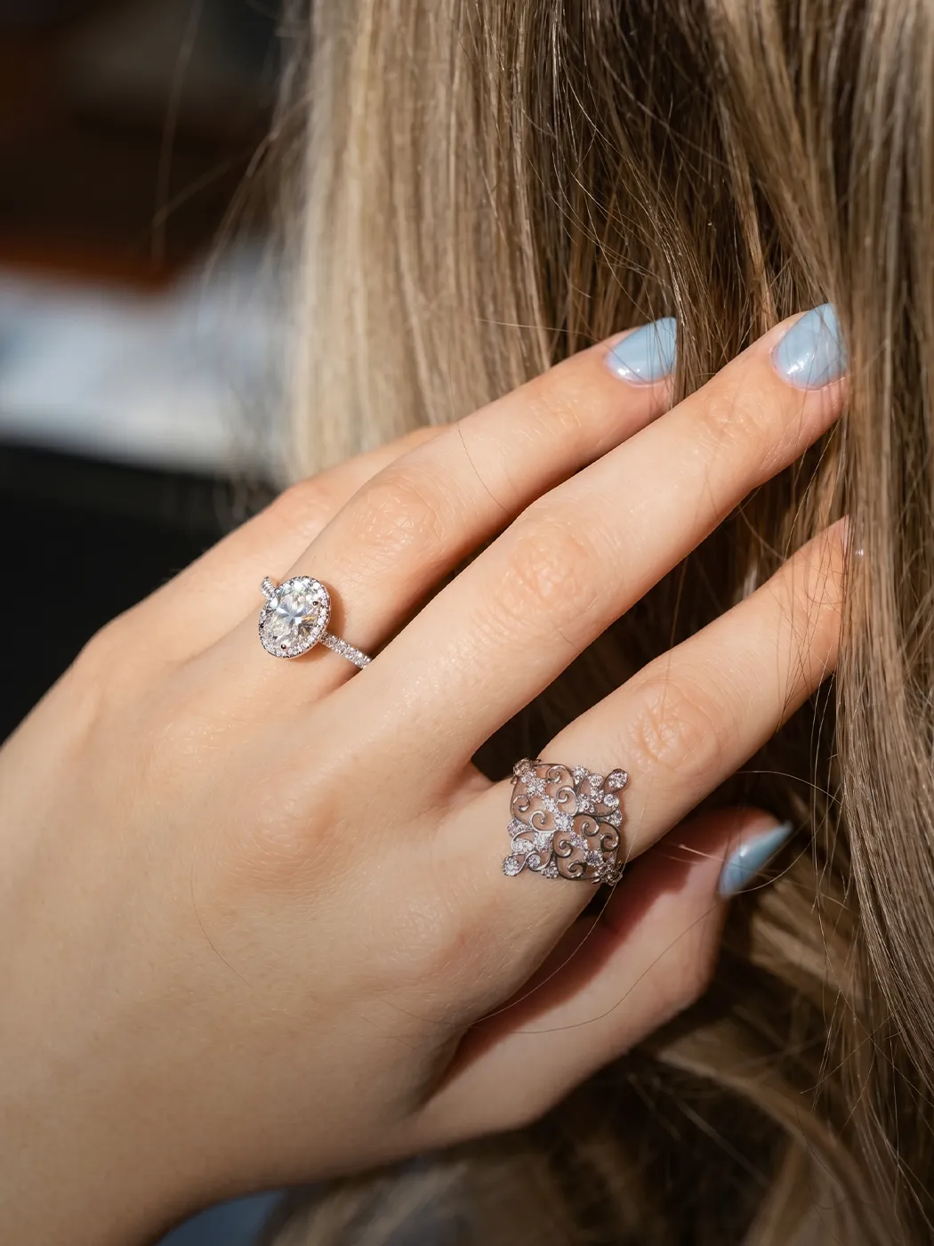 Hand with two diamond rings, one round and one ornate, against hair background.