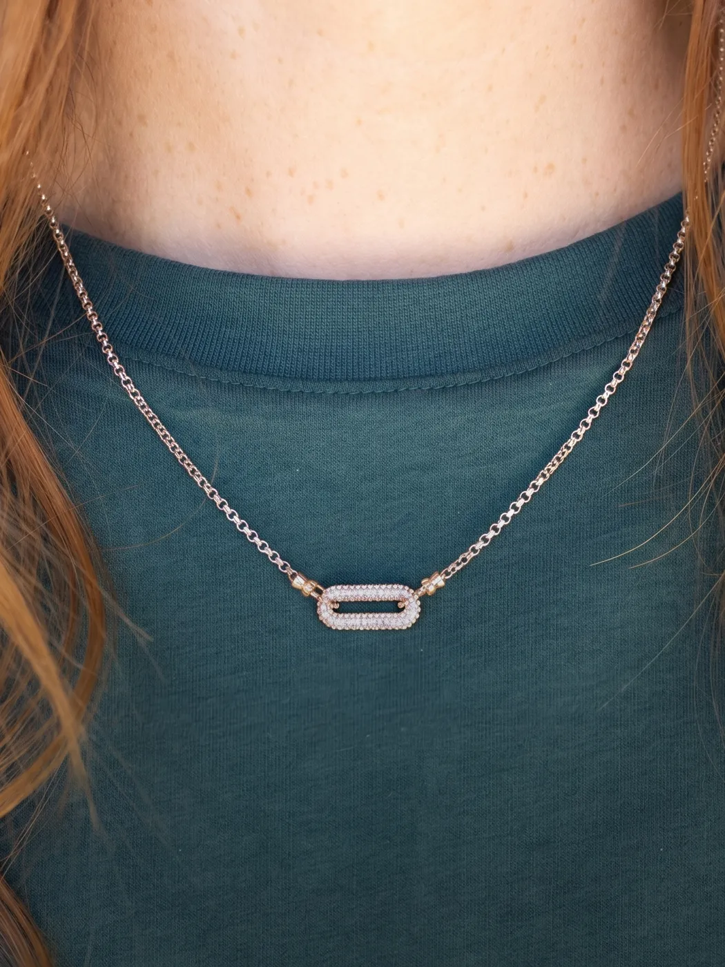 A person wearing a delicate chain necklace with a diamond-studded oval pendant.
