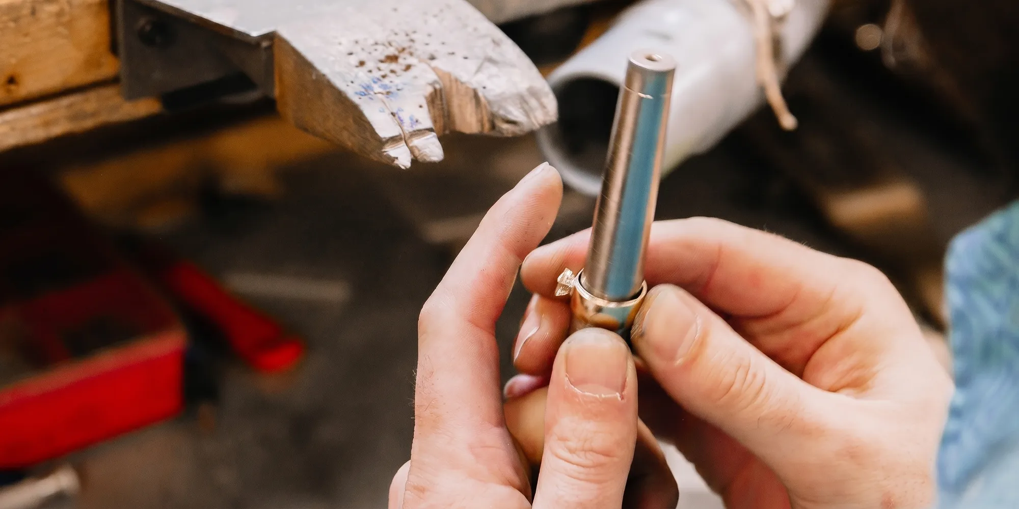 Hands crafting a ring with a metal tool on a workbench.