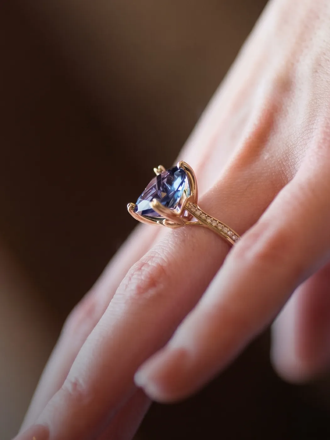 A hand wearing a gold ring with a large blue gemstone.