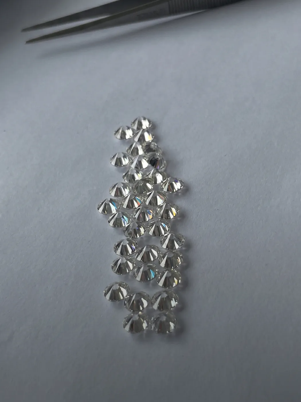 A collection of loose diamonds on a white surface with tweezers nearby.