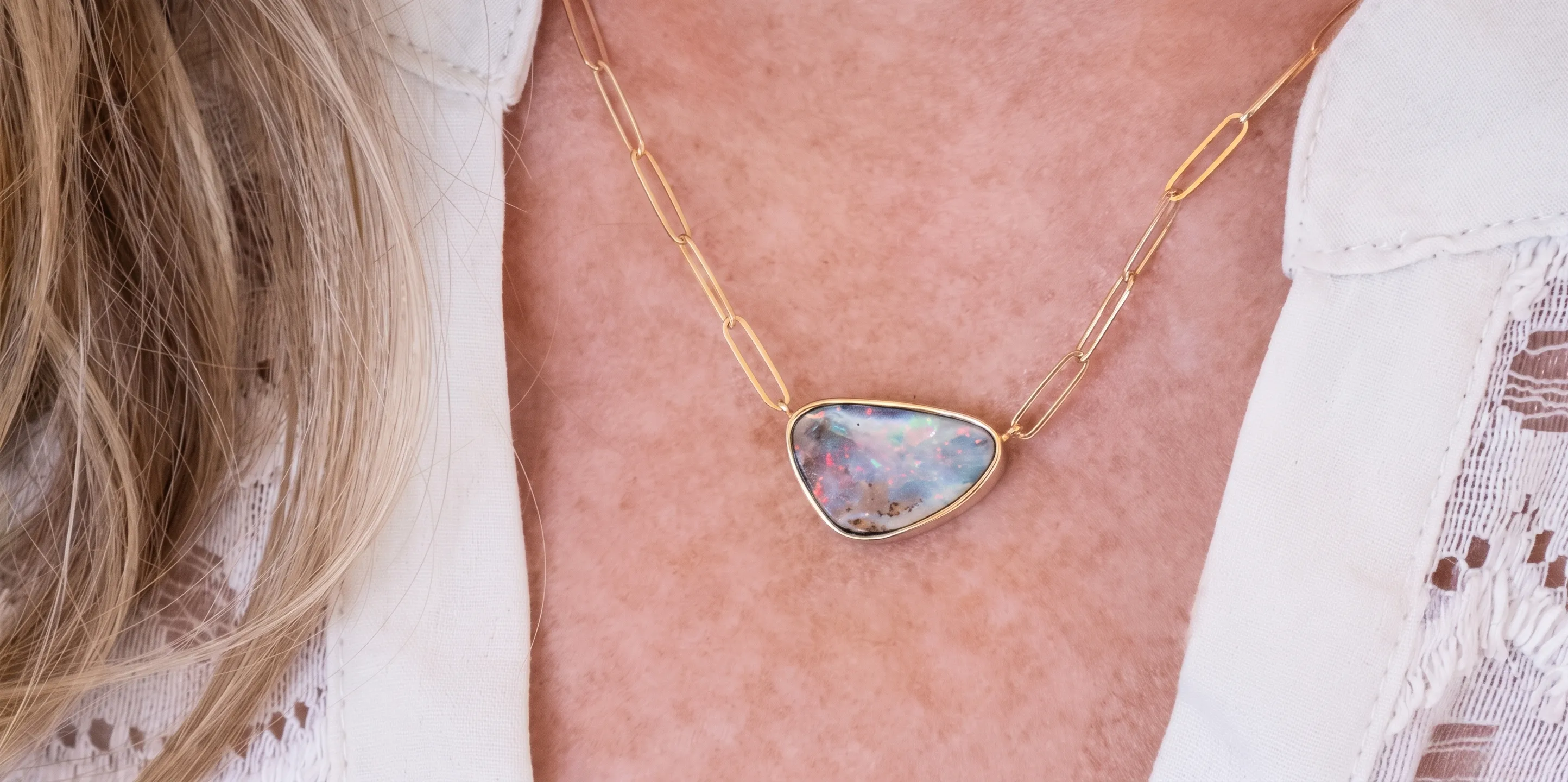 Close-up of a hand holding a gold chain with a blue gemstone pendant and wearing a gold ring with a clear stone.