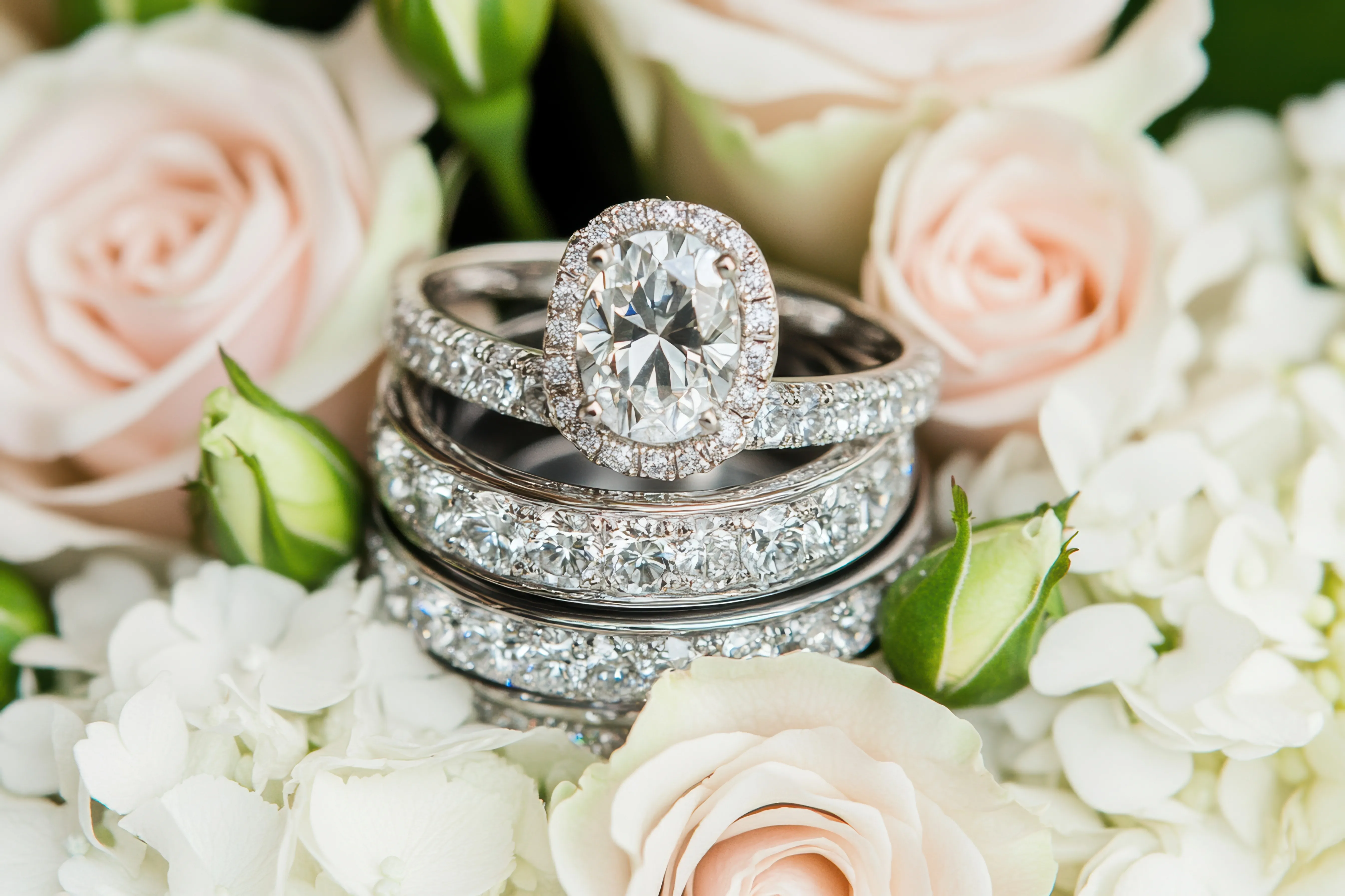 Engagement rings displayed among soft pink roses and white flowers. Click to shop now at Monarch Jewelry in Winter Park.