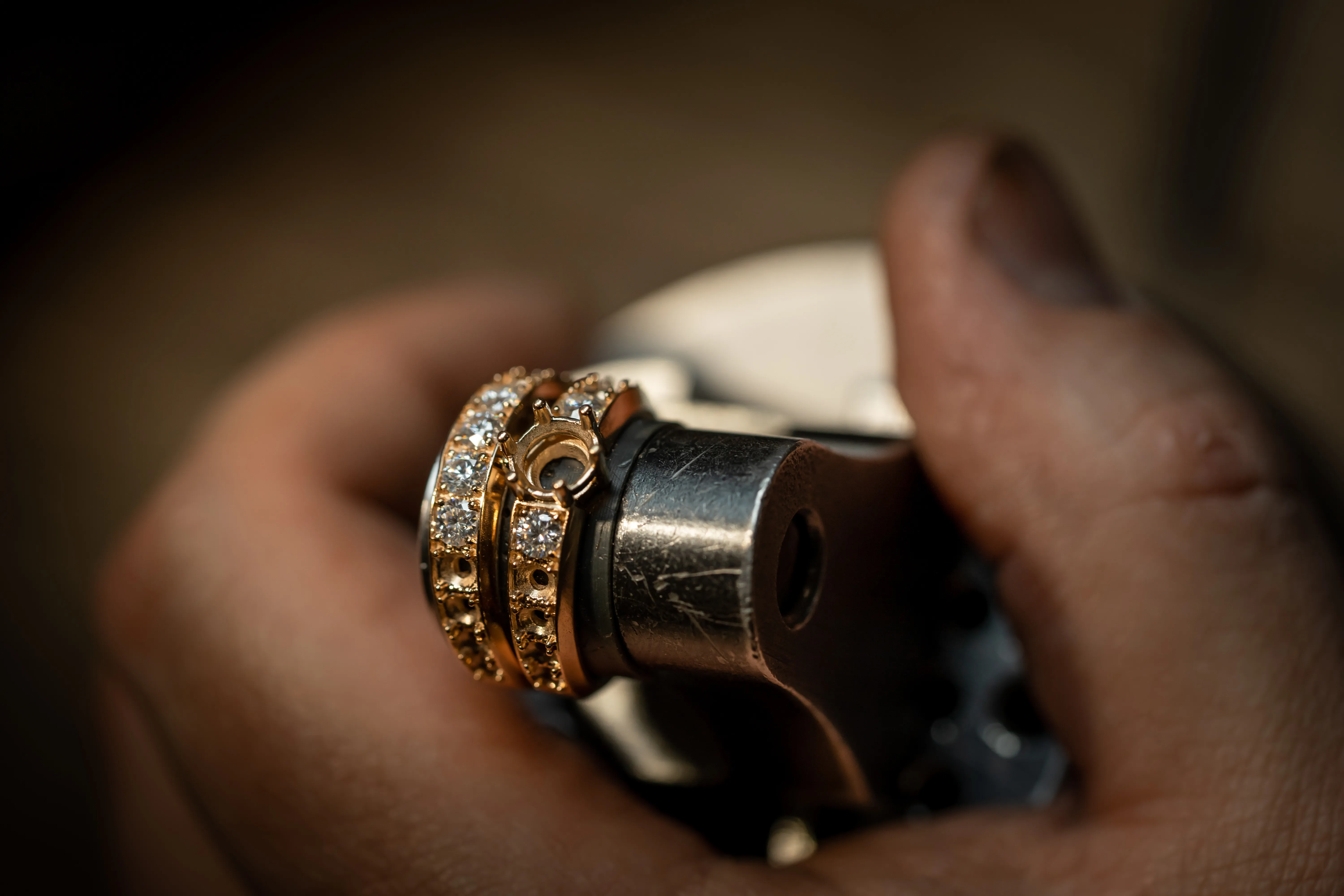 A hand holding a gold ring with diamonds, working on a jewelry tool at Monarch Jewelry in Winter Park.