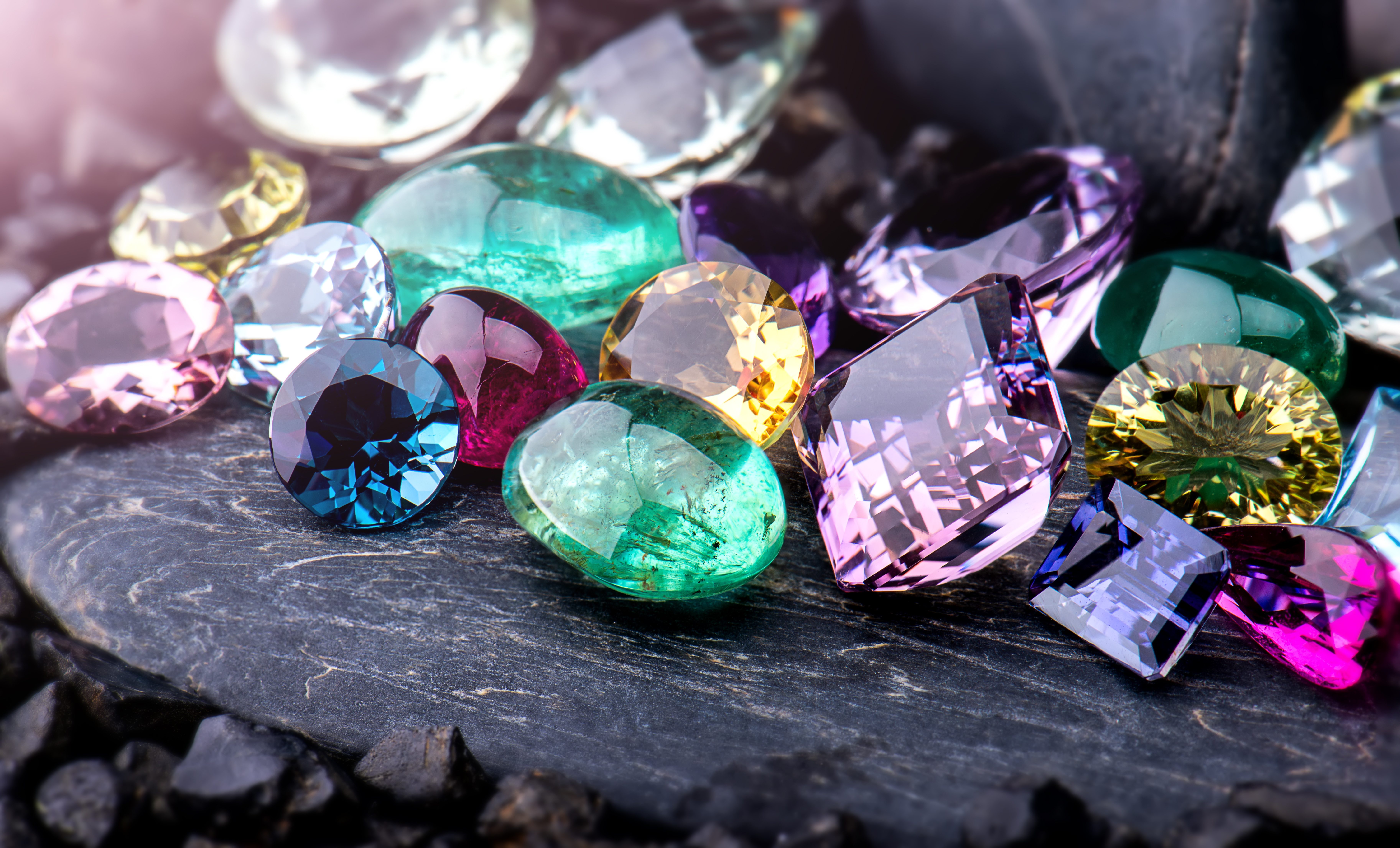 Colorful gemstones scattered on a dark surface. Click to shop now at Monarch Jewelry in Winter Park.